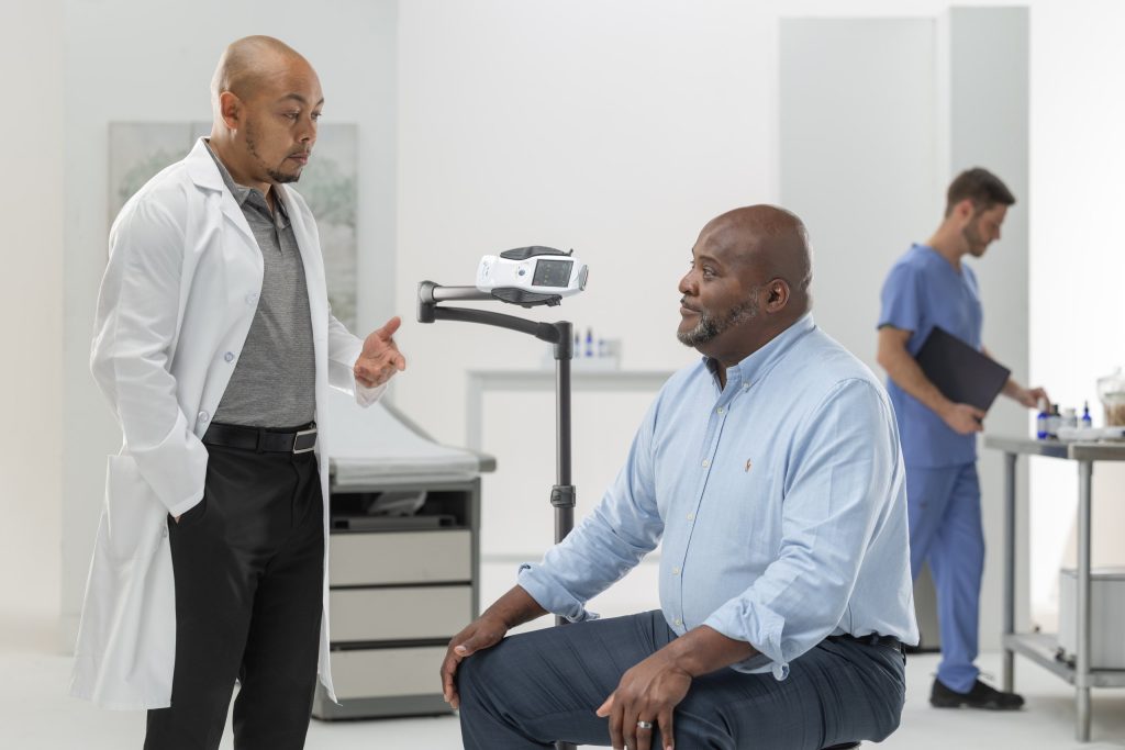 Practitioner discussing cold laser therapy with a seated patient beside a PTL PRO device mounted on an articulating stand