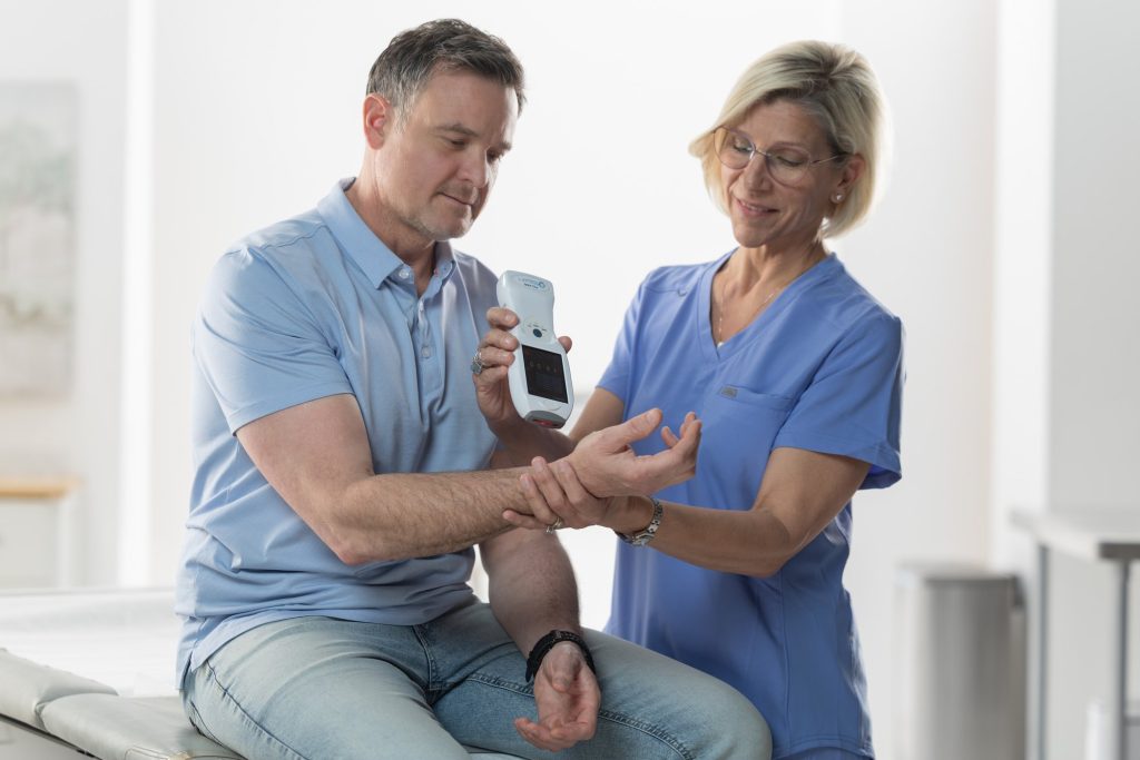 A clinician in scrubs holding the handheld PTL PRO over a seated patient forearm during a short treatment